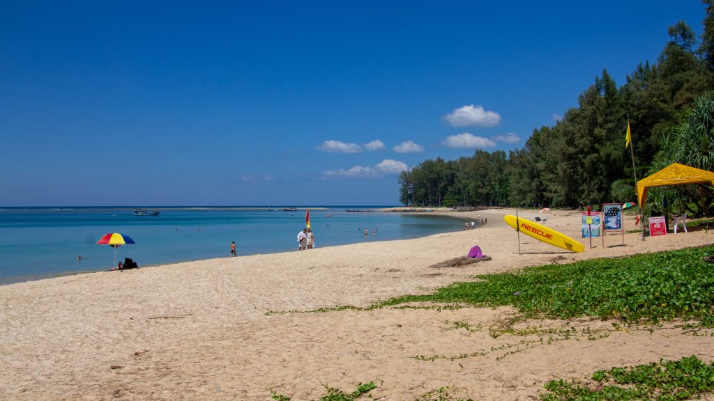 Shaded shoreline lined with casuarina trees at Nai Yang Beach Phuket, with shallow waves reaching the sand.