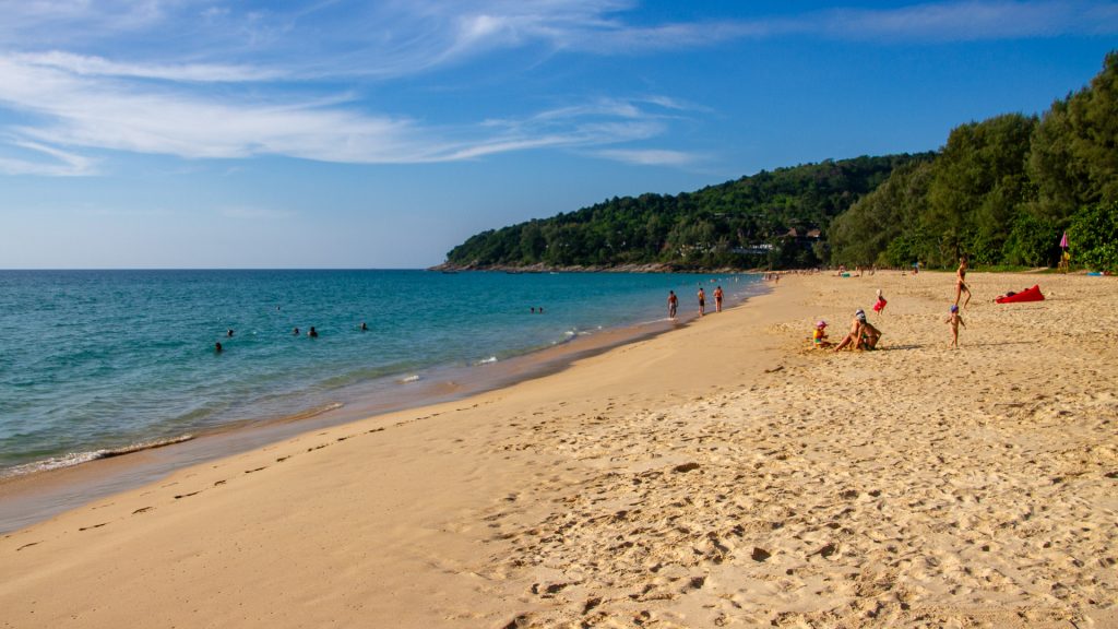 Naithon Beach Phuket wide sandy bay with casuarina trees and hillside villas above the turquoise Andaman Sea.
