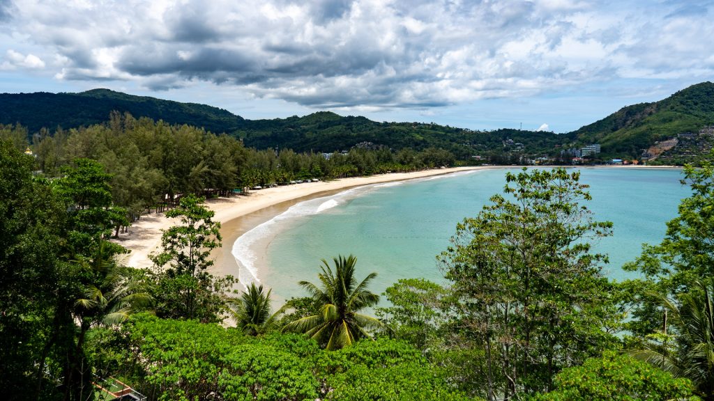 Central shoreline of Kamala Beach Phuket with soft sand and calm dry-season water.