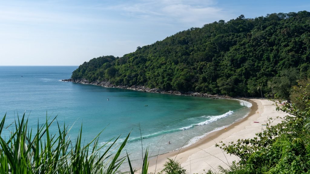 Karon Noi Beach Phuket enclosed white sand cove with calm turquoise water, forested hillside, and gentle shoreline waves