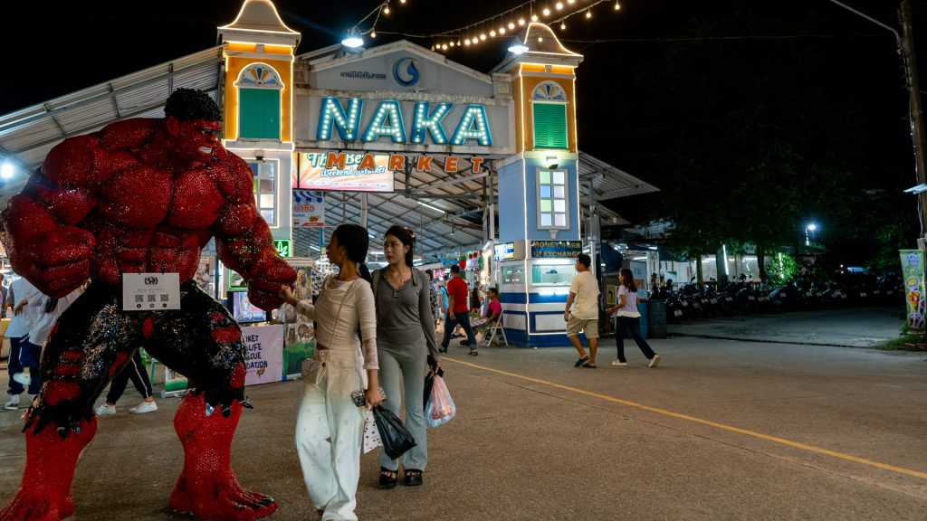 Naka Weekend Market Phuket entrance area with a large red character figure and pedestrians walking past