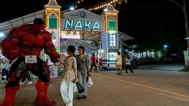 Naka Weekend Market Phuket entrance area with a large red character figure and pedestrians walking past