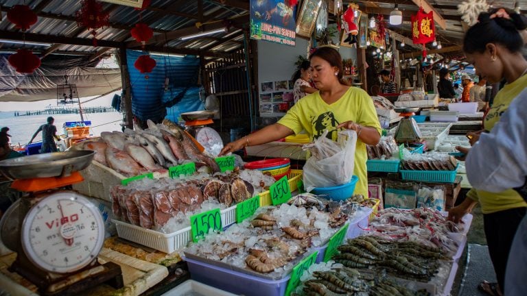 Vendor assembling a large seafood order into bags at Rawai Seafood Market, indicating bulk purchasing for cooking or resale.
