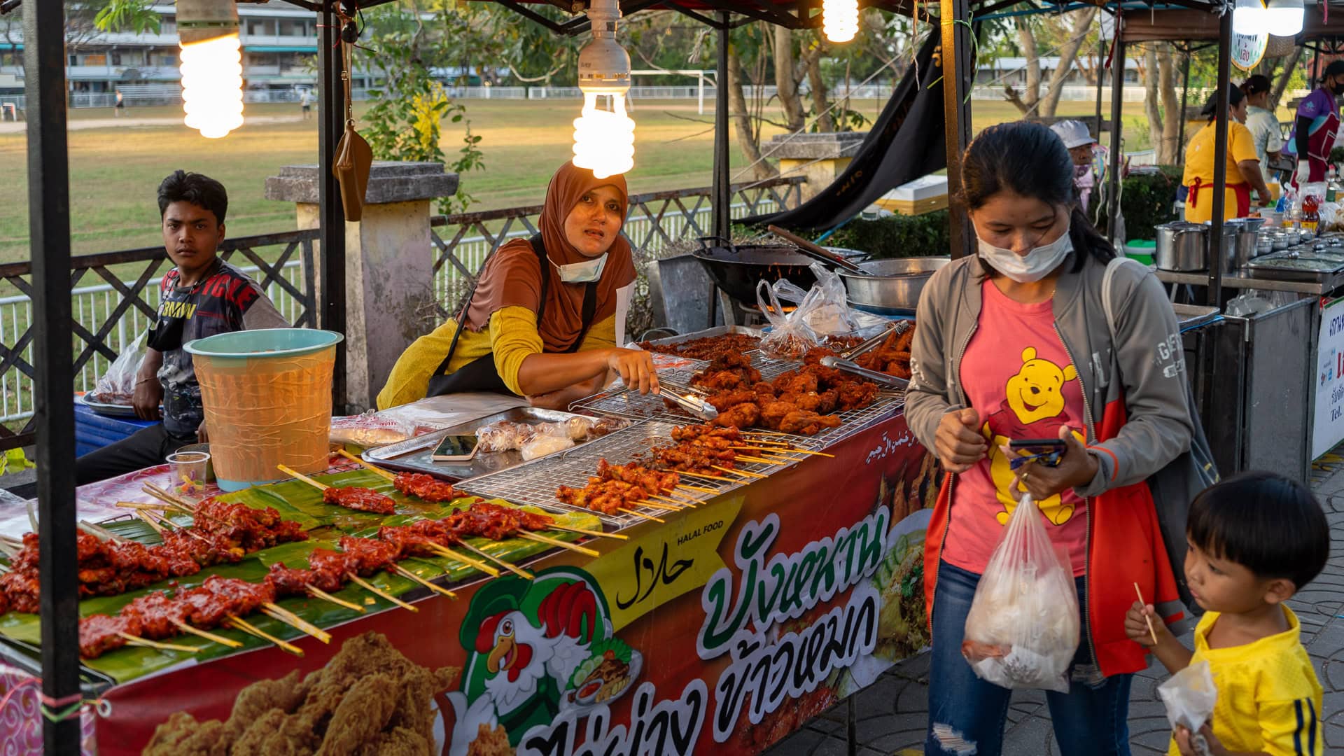 Family standing at a grilled skewer stall at Chaeng Talay Street Food Market during early evening hours.