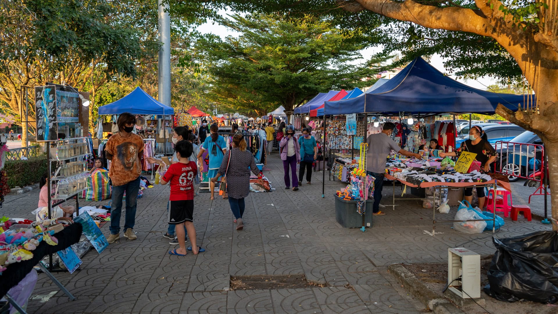 Non-food stalls selling clothes and household items at Chaeng Talay Street Food Market along a shaded pedestrian path.