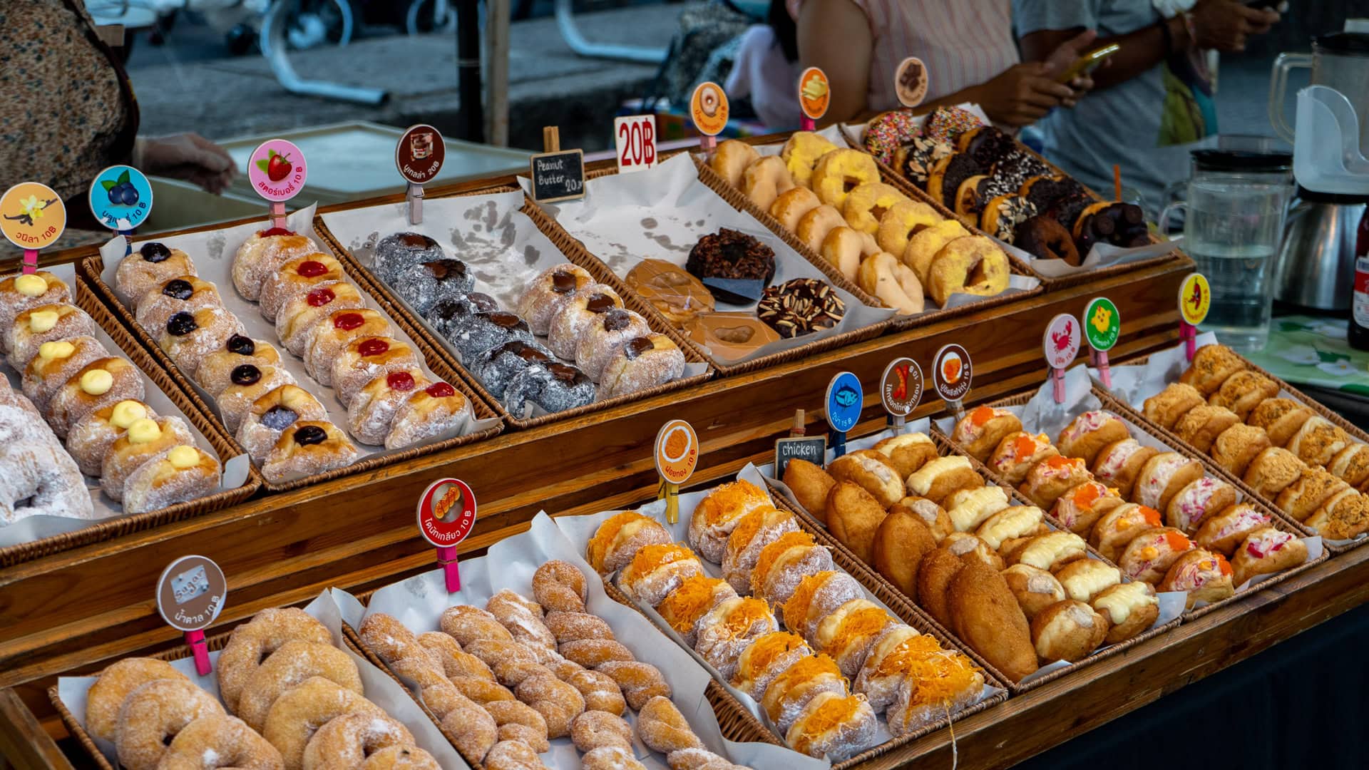 Dessert stall with donuts and filled pastries at Chaeng Talay Street Food Market displayed on tiered trays.