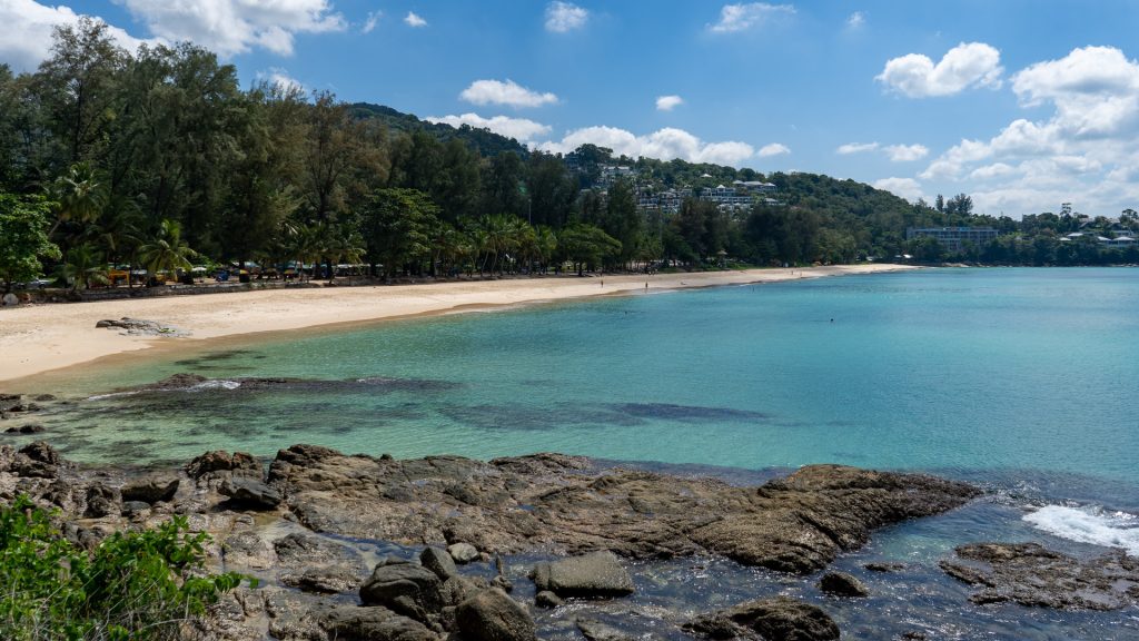 Mid-beach view toward northern headland with resort buildings visible.