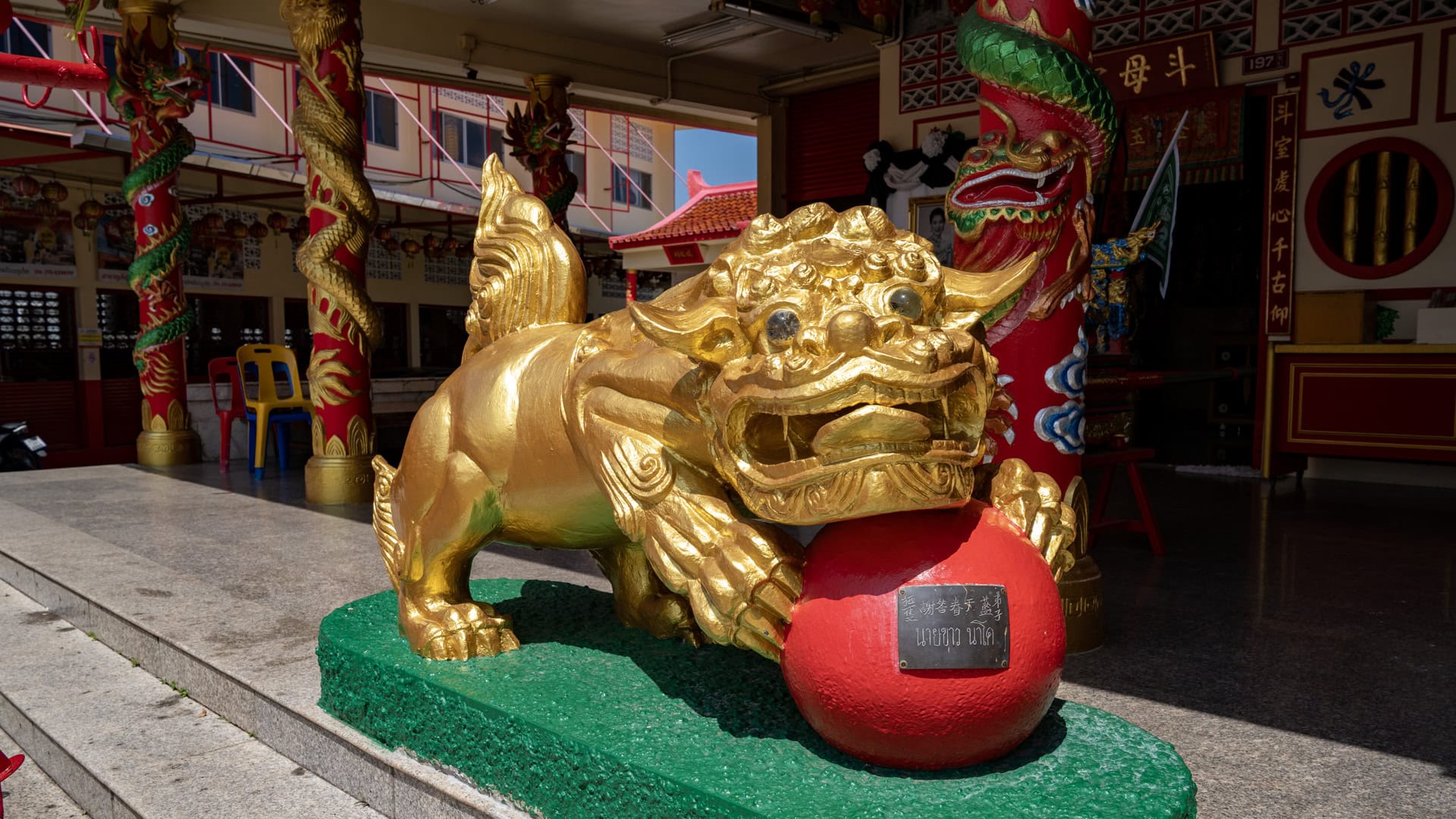 Close view of a gold guardian beast statue holding a red ball near the entrance steps of Bang Neow Shrine.