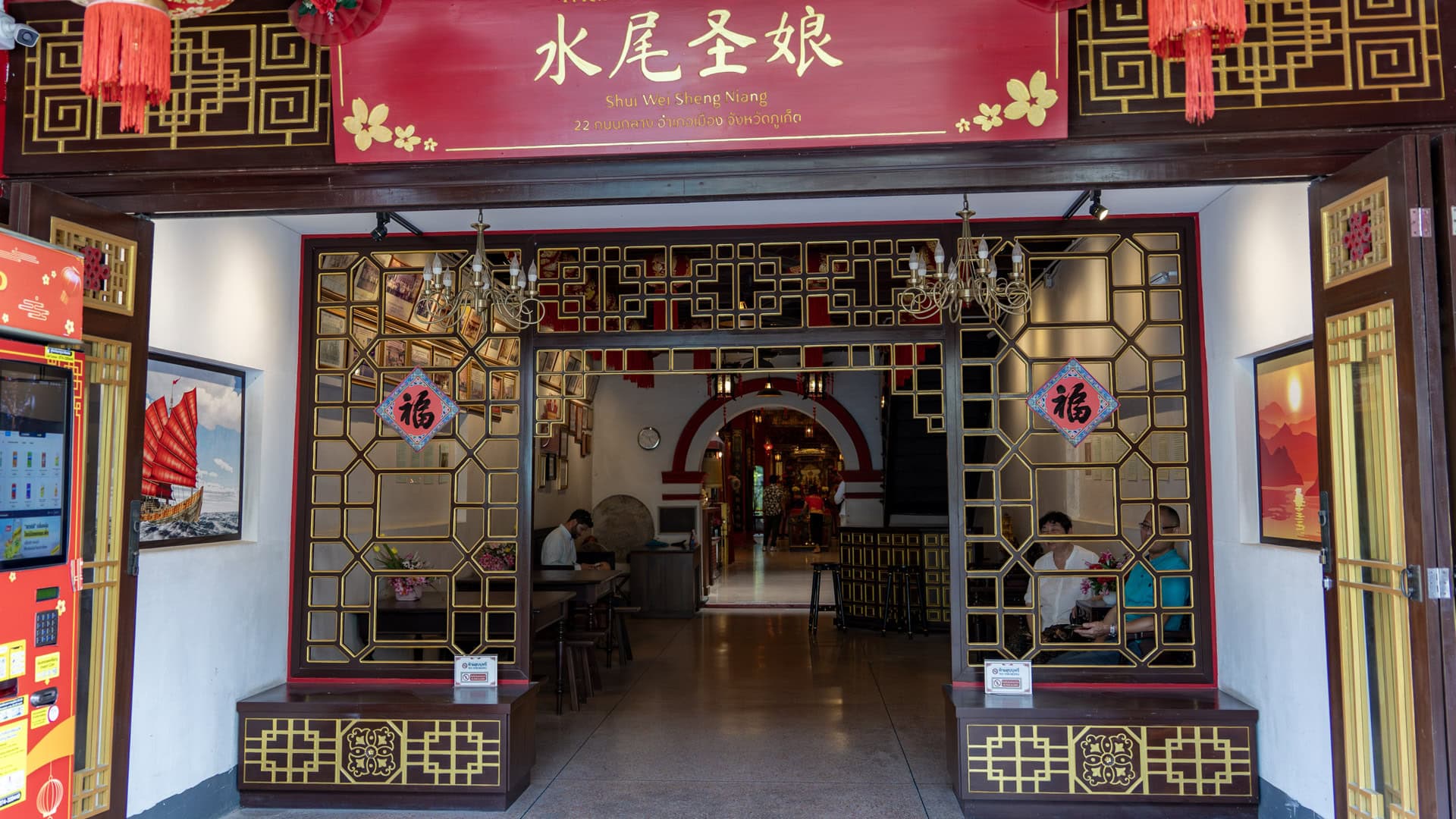 The entrance hall of San Chao Hainan is framed by black-and-gold lattice screens, red lanterns, and a signboard above the doorway.