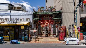 The entrance gate to San Chao Saengtham stands between commercial buildings, with red lanterns hanging inside the passage and a road in front.