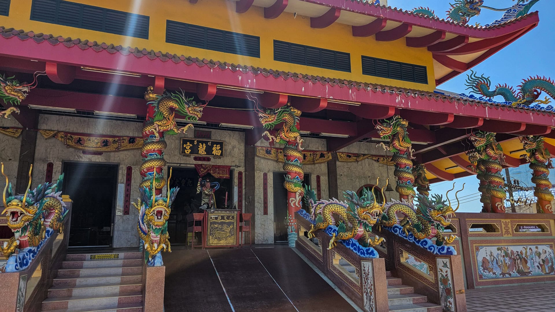 The front veranda at San Chao Tha Ruea has dragon-wrapped columns, paired stairways, and a central platform beneath a yellow upper wall.