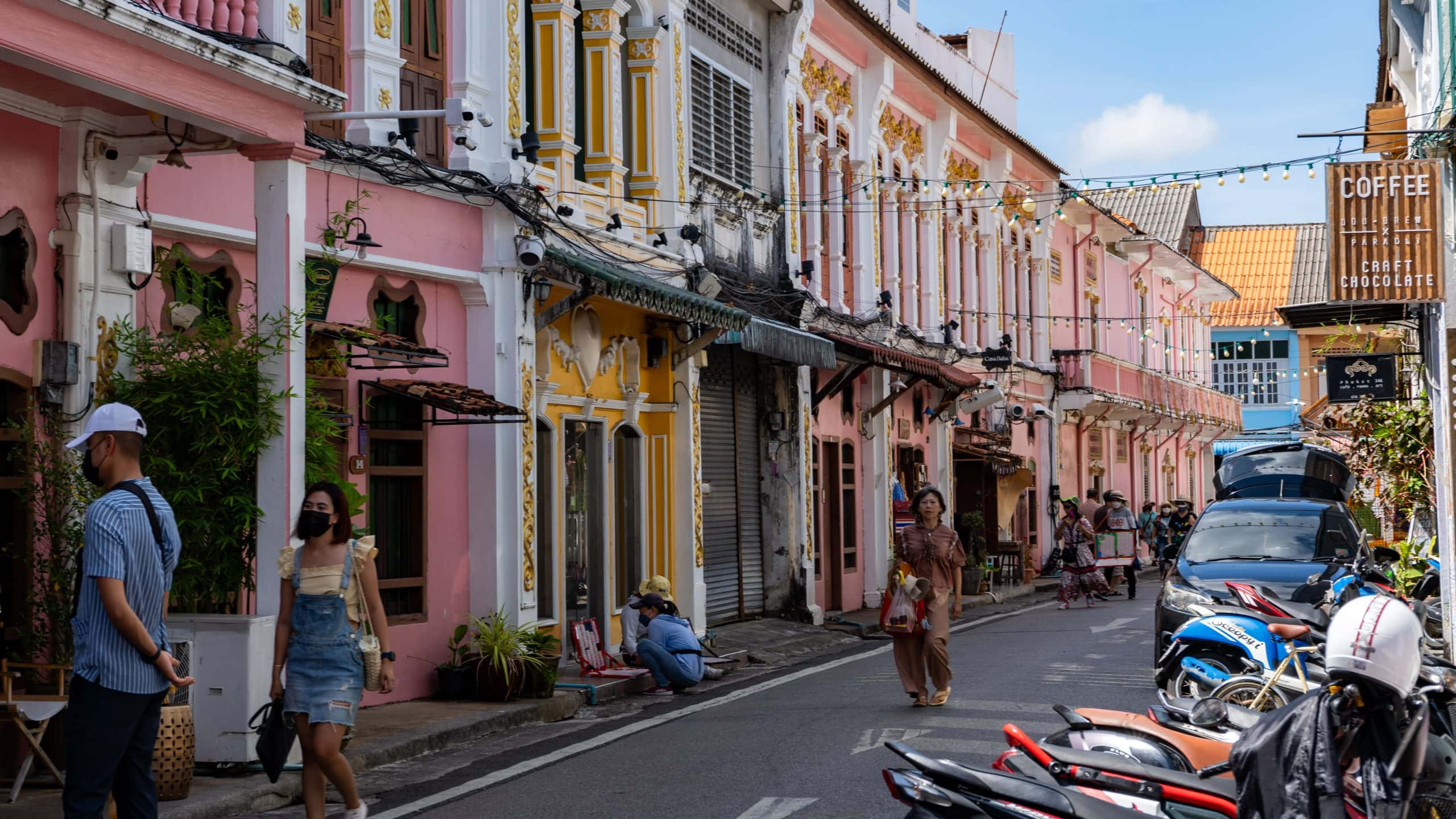 People walking through a street of colourful historic shophouses in Phuket Old Town