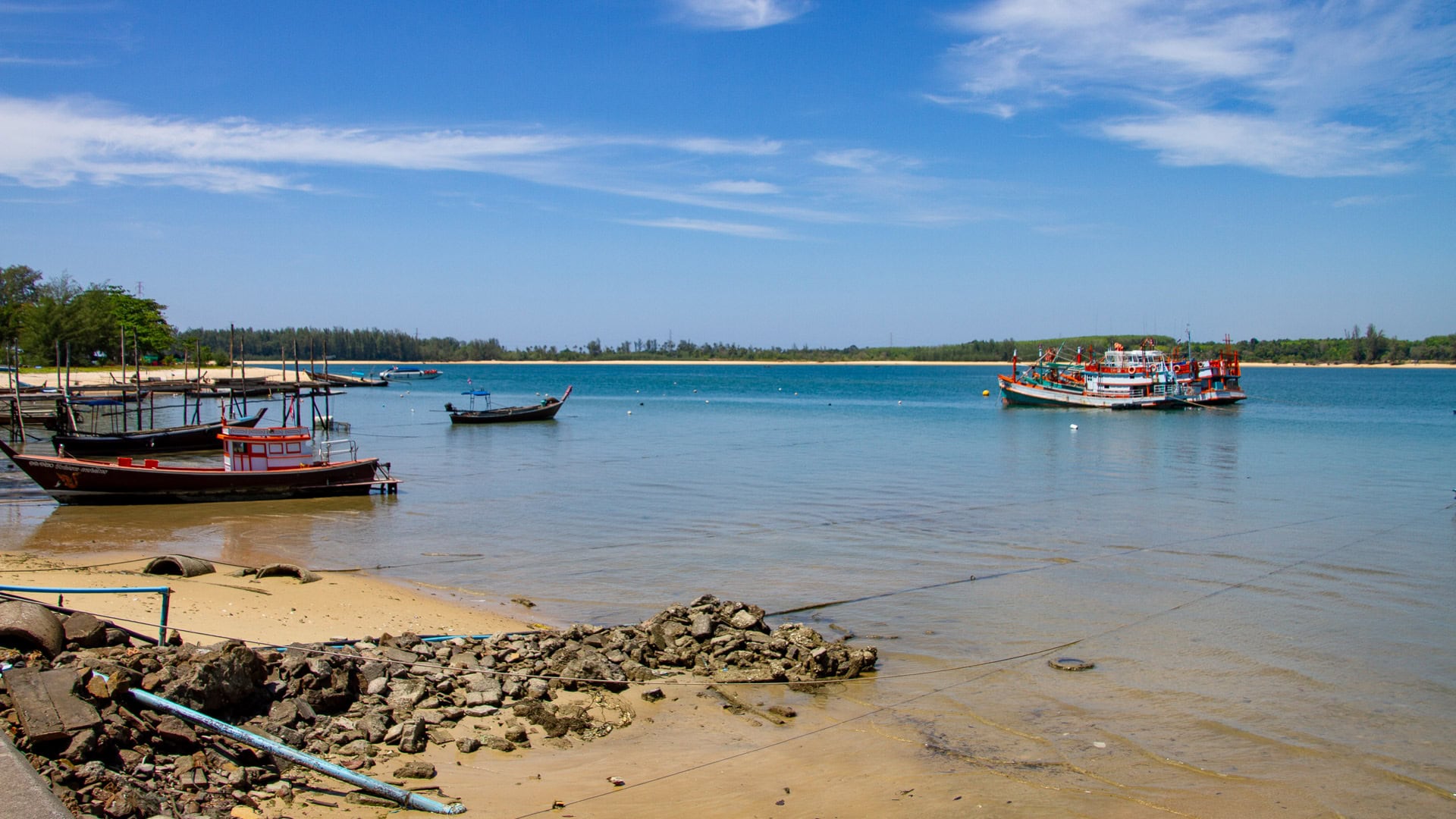 Fishing boats anchored near the shoreline at Haad Pak Phra Beach, Mai Khao, Phuket, with sand flats visible at low tide.