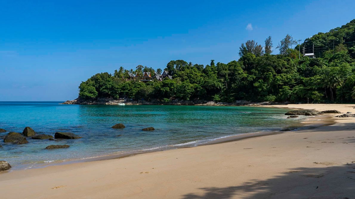 Northern perspective of Laem Singh Beach Phuket with forested slopes and clear water.