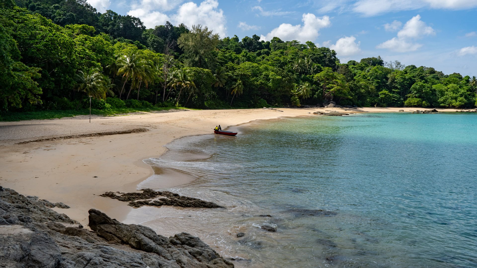 Wide view of Laem Singh Beach Phuket with shallow water and a small boat near the shoreline.