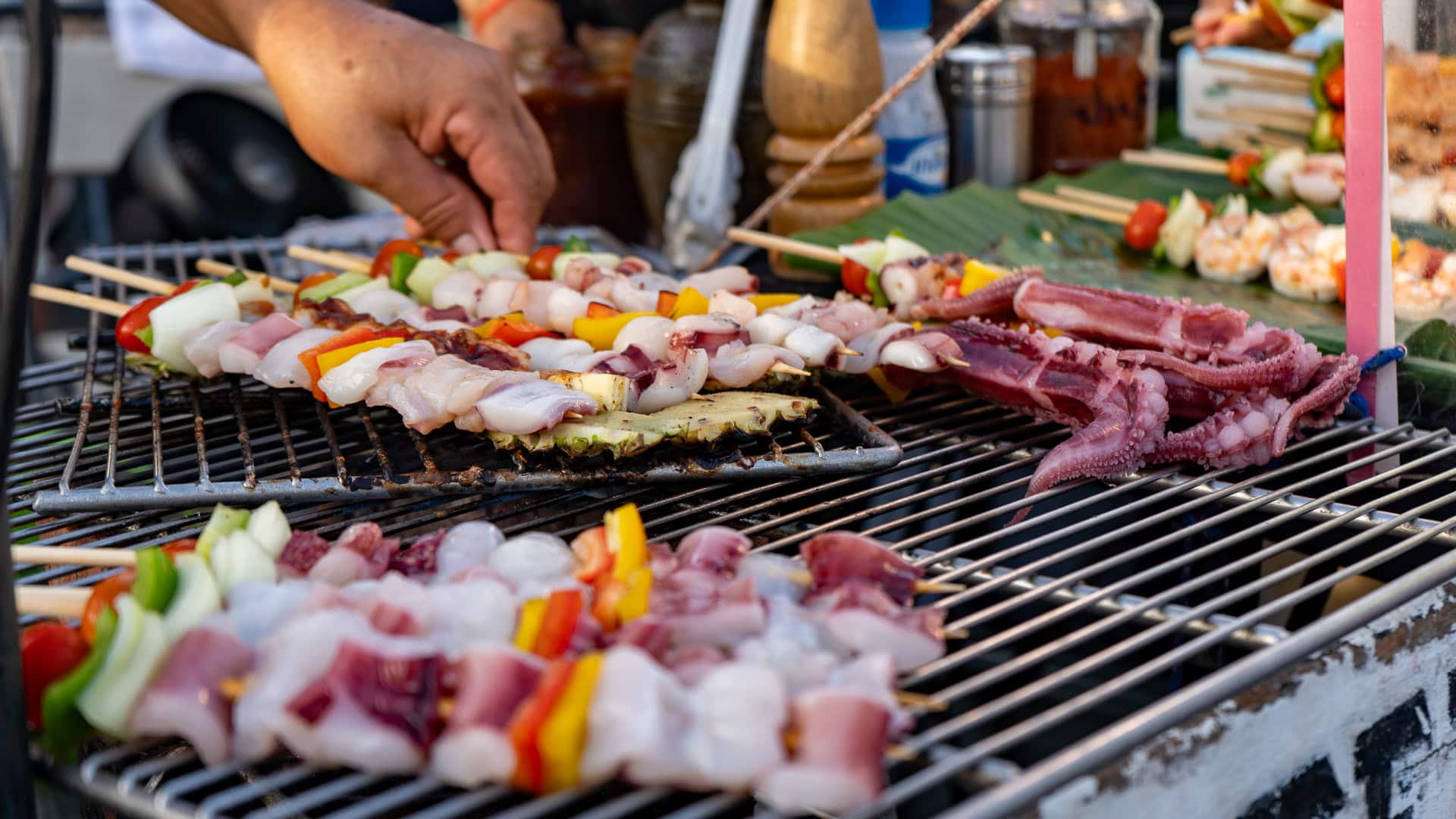 You watch the squid turn on the grill, threaded with vegetables, nudged closer to the heat, checked by hand, then turned again until the surface tightens and the edges begin to colour.