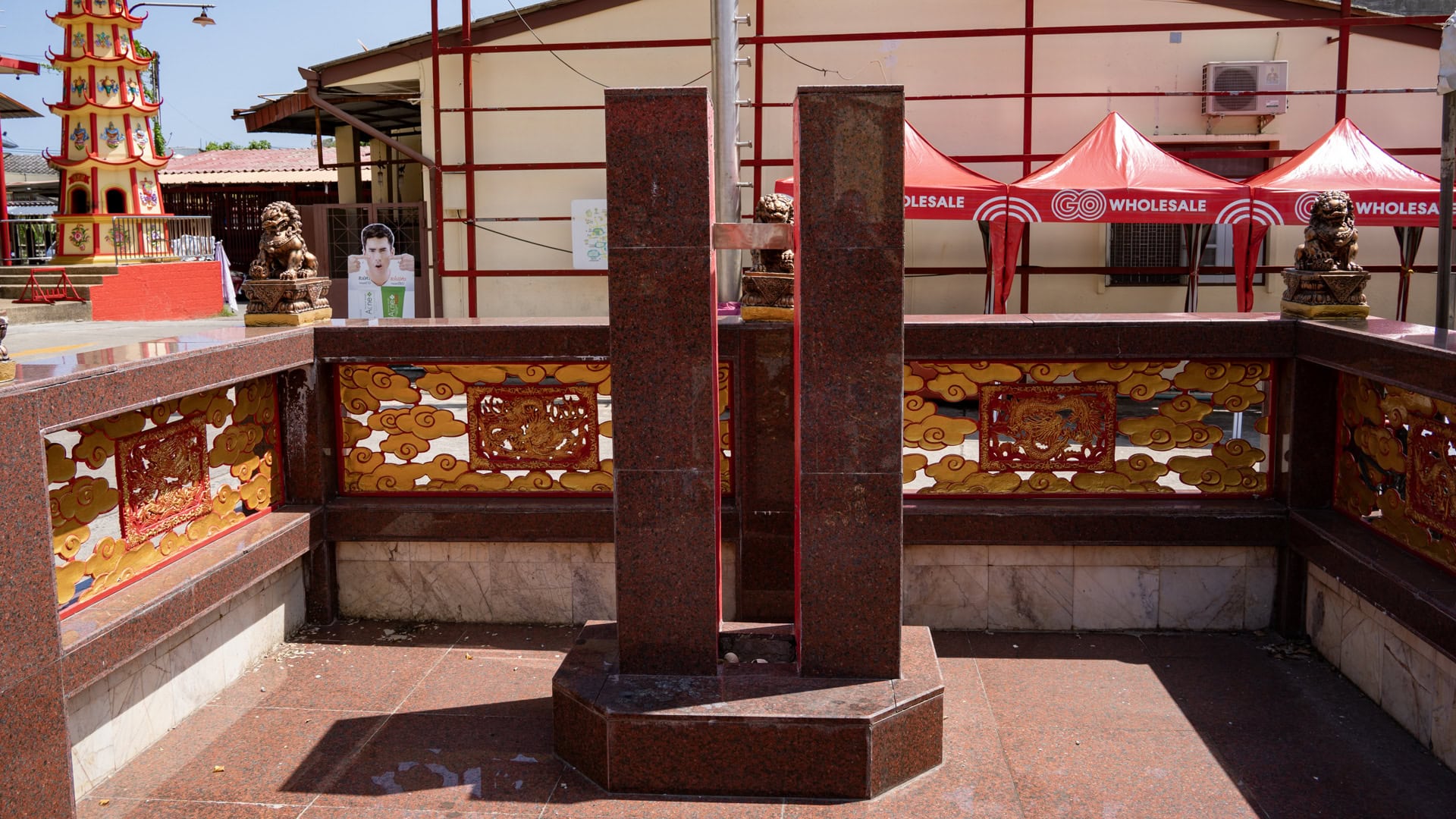 Polished red stone ceremonial poles standing inside a low decorated enclosure with cloud-and-dragon panels at Bang Neow Shrine.