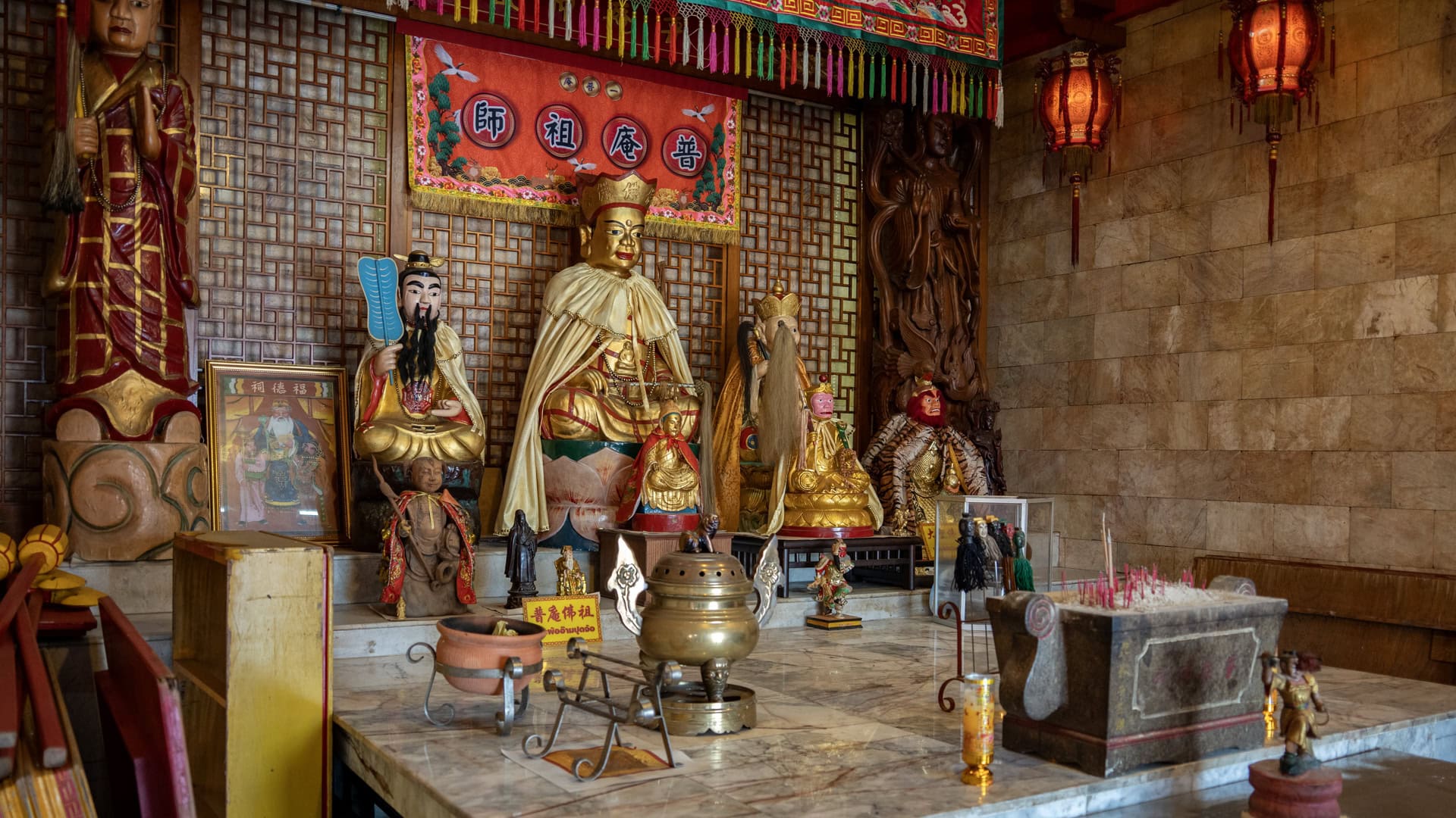 Main altar inside Bang Neow Shrine with seated figures, incense burner, red hanging lanterns, and a marble platform.