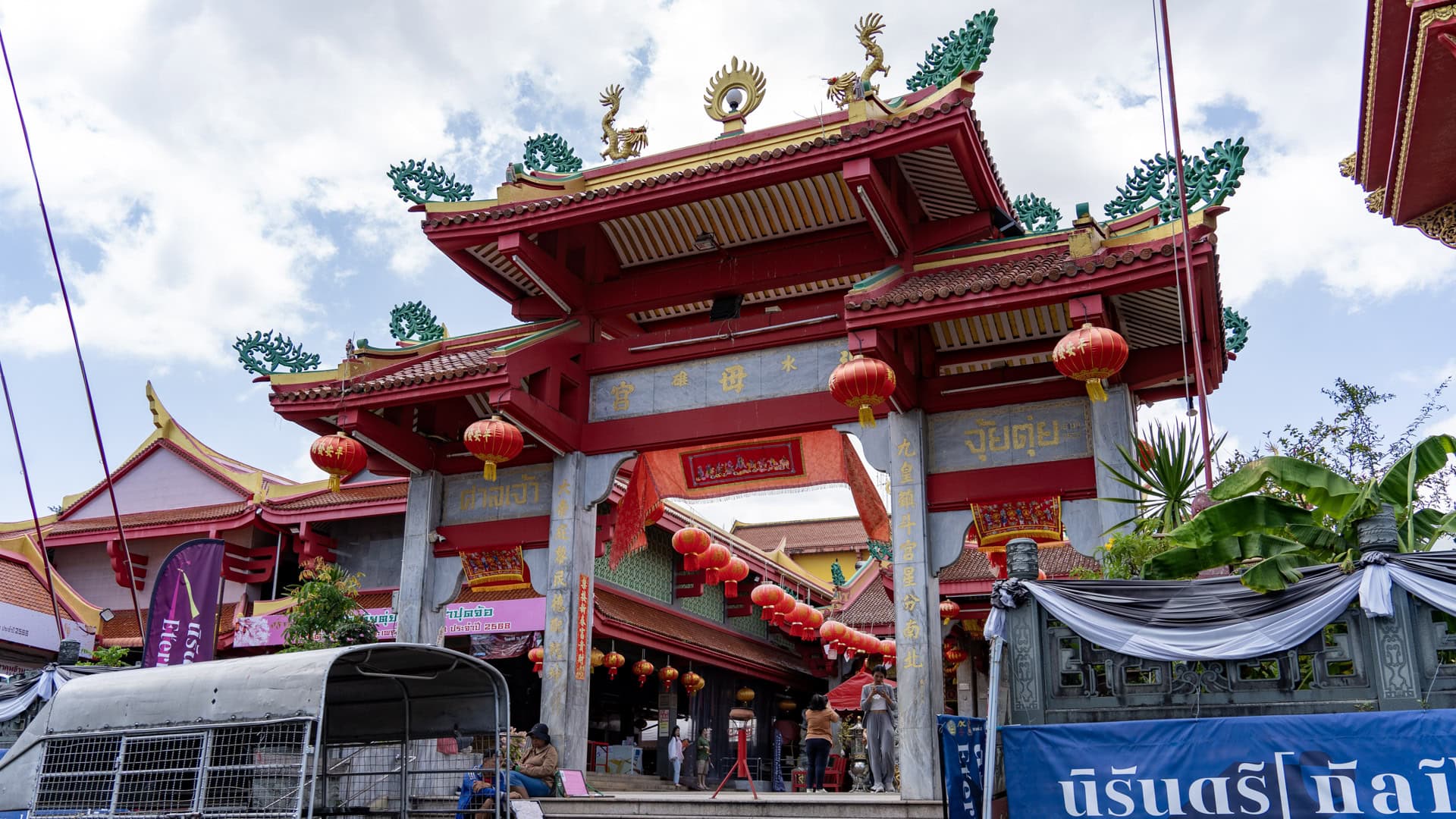 The main entrance gate at San Chao Jui Tui is painted red and hung with red lanterns, with gold-lettered plaques and roof ornaments above the passage into the compound.
