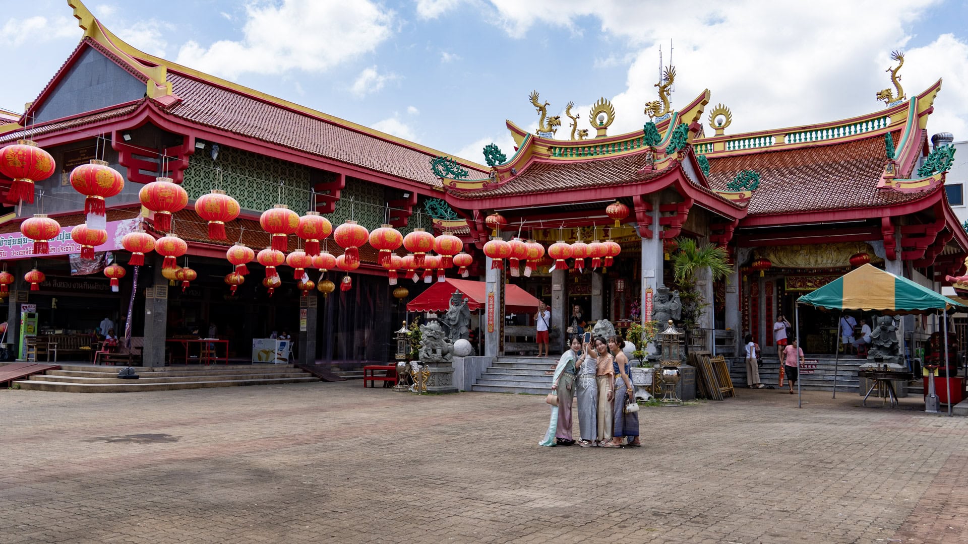 A broad paved courtyard at San Chao Jui Tui faces a red-roofed shrine hall decorated with hanging lanterns, while four women pose for a photo near the centre.