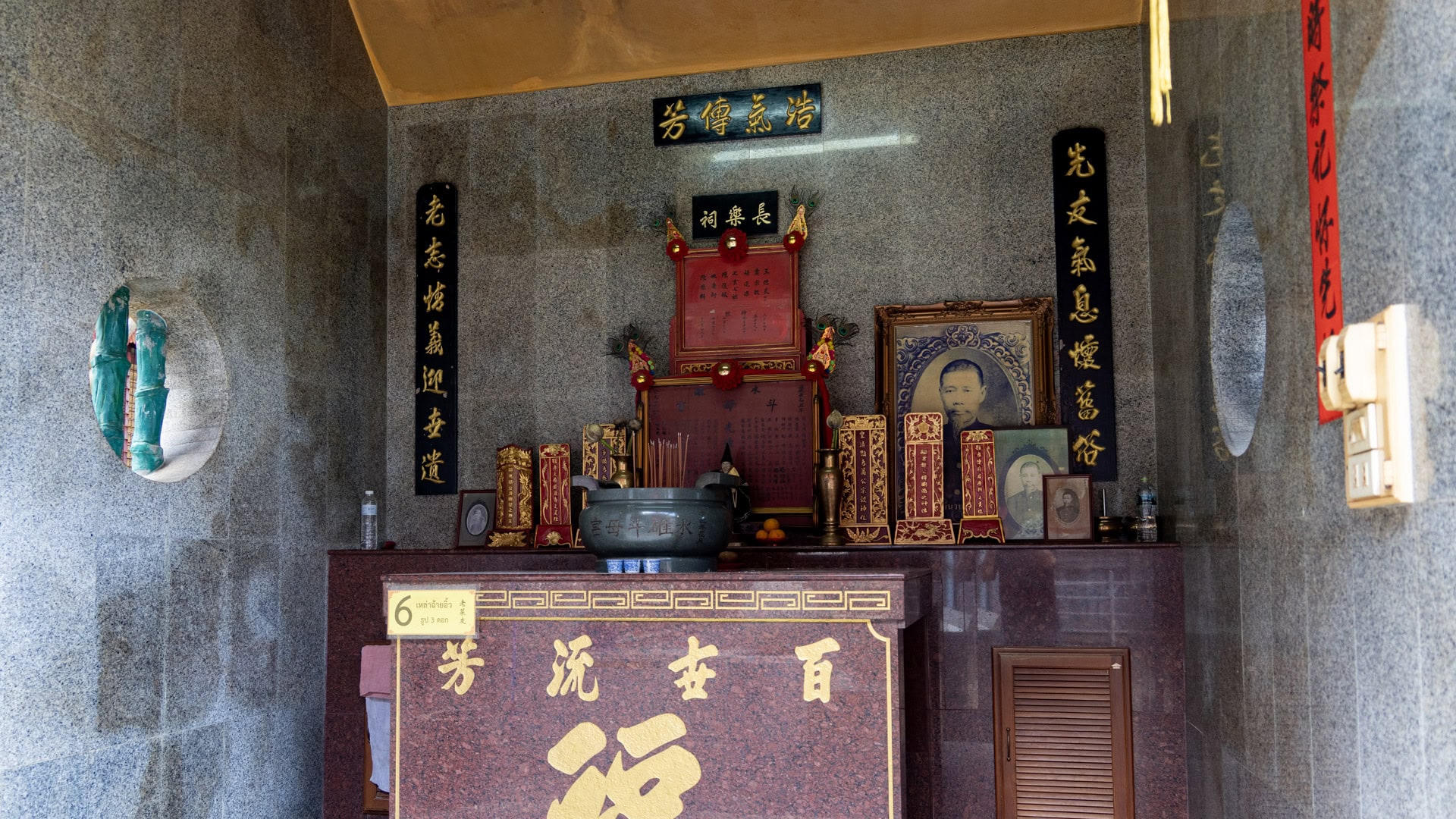 A memorial altar at San Chao Jui Tui stands inside a granite-lined niche, with framed portraits, incense, red tablets, and black calligraphy plaques around a central incense urn.