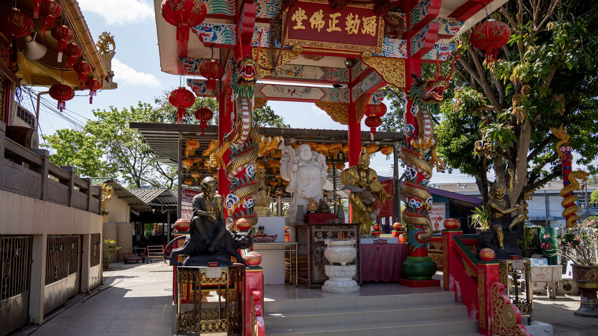 A red entrance arch at San Chao Kiew Tien Keng is wrapped with dragon columns and hung with red lanterns, with white and gold statues visible inside.