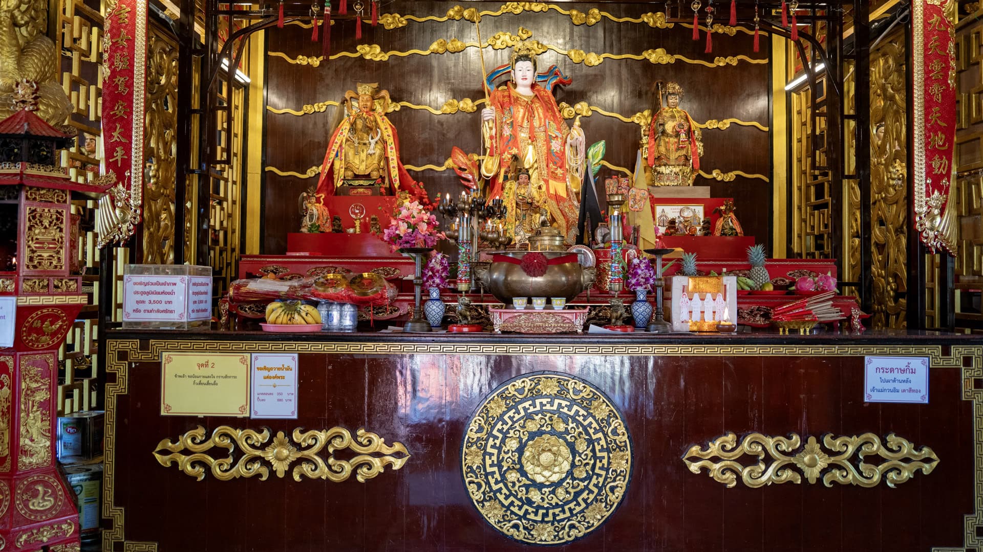 The main altar at San Chao Kiew Tien Keng displays a central deity figure in red and gold robes, with offerings, incense vessels, and smaller figures arranged across the front.