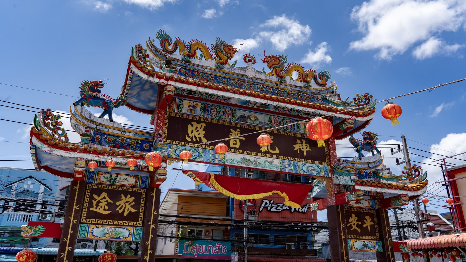 Entrance arch at Sam Kong Shrine with gold Chinese characters, red lanterns, dragon figures, painted panels, and street wires behind it.