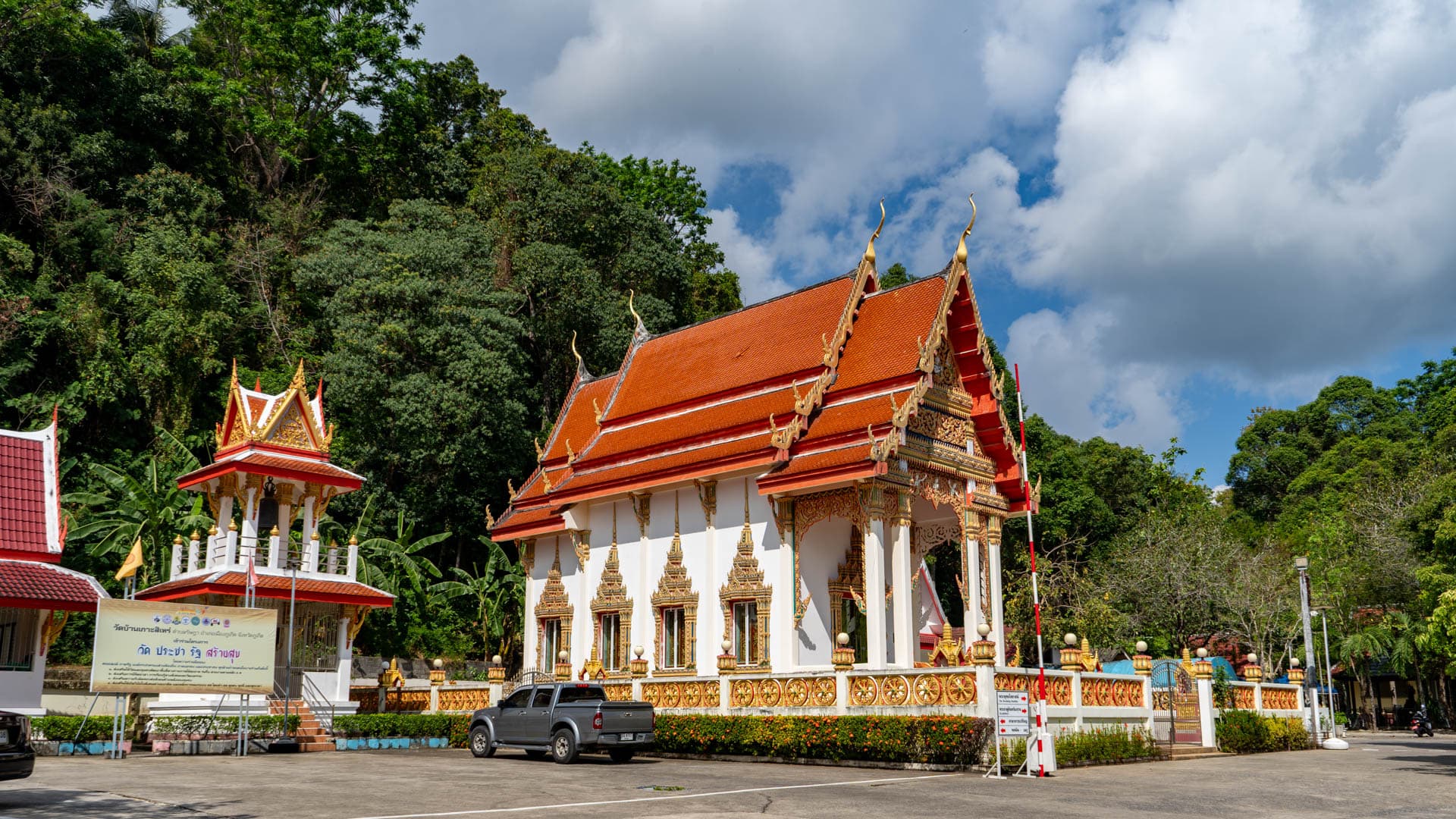 Red-roofed ordination hall at Wat Ban Koh Sirey beside forested hillside