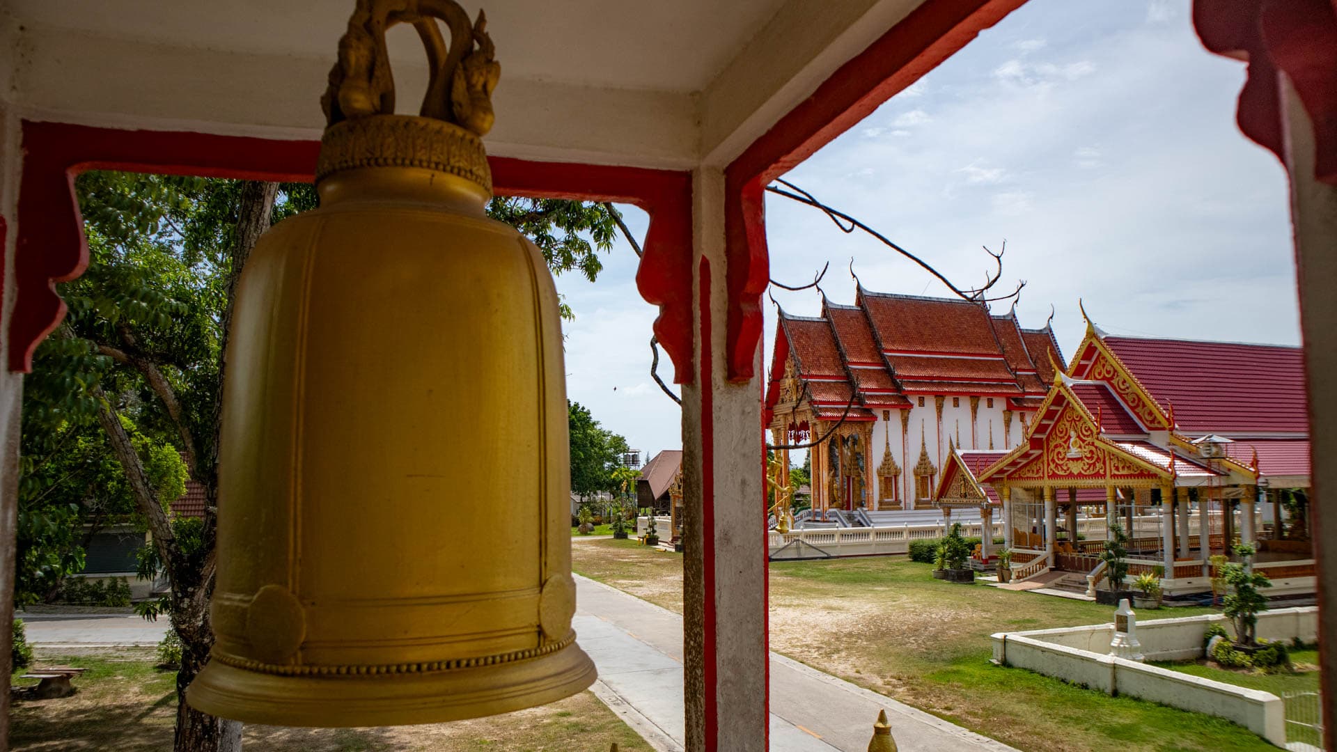 Temple bell inside pavilion overlooking Wat Chalong ordination hall and courtyard
