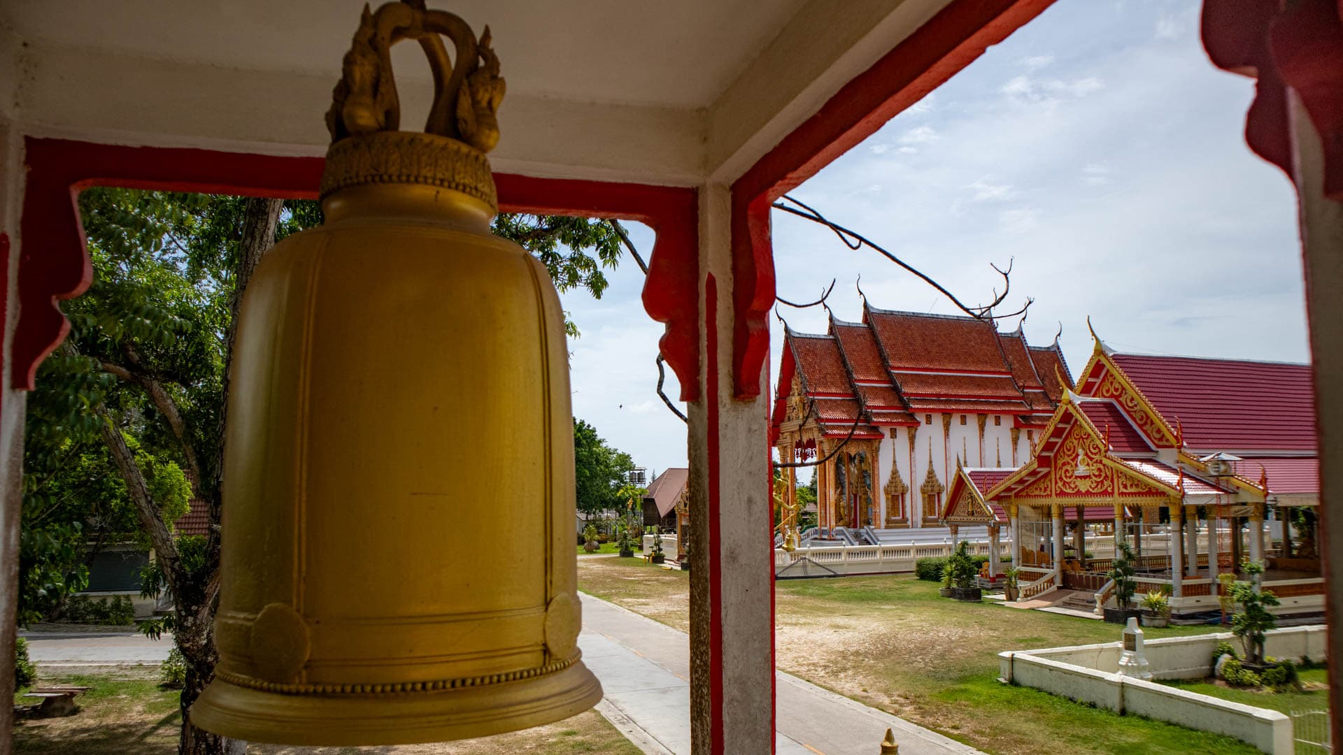 Temple bell hanging in pavilion overlooking courtyard and ordination hall at Wat Choeng Thale