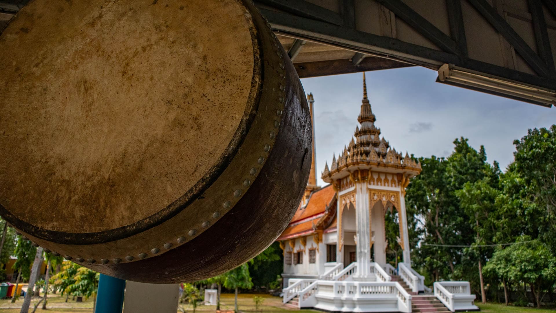 Funeral drum hanging beneath shelter beside cremation pavilion at Wat Choeng Thale