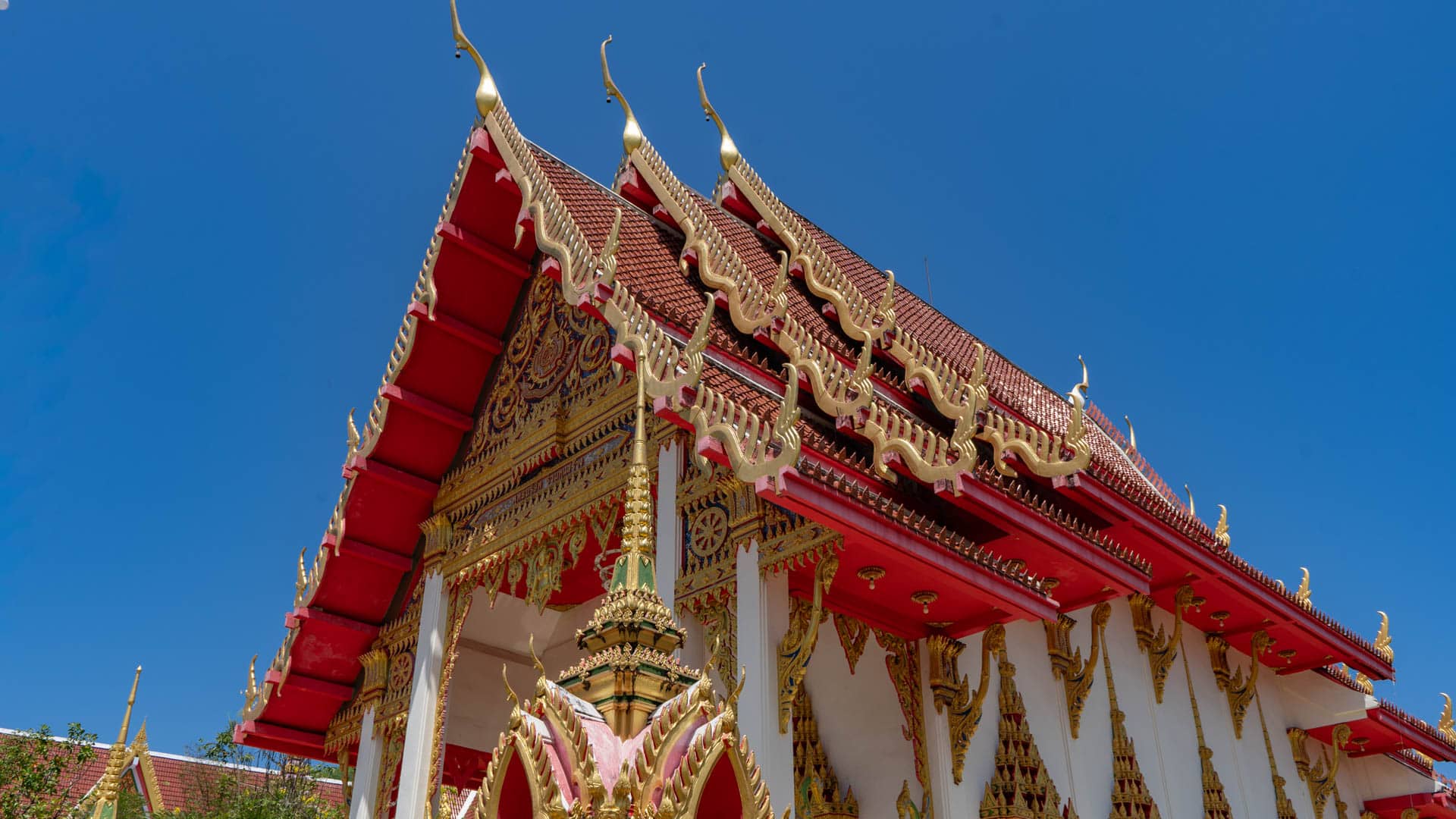 Corner view of Wat Karon viharn with red roof and decorative columns
