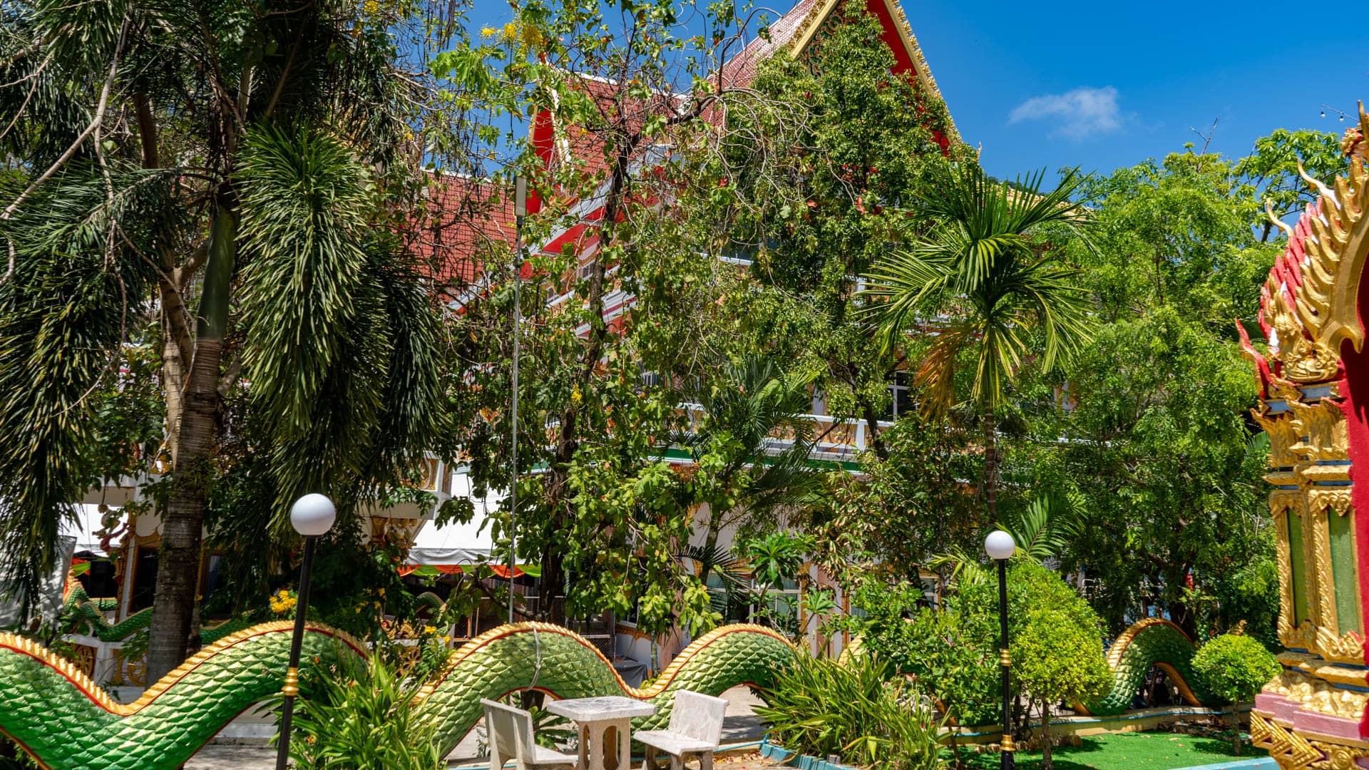 Green naga wall winding through garden area at Wat Karon temple grounds