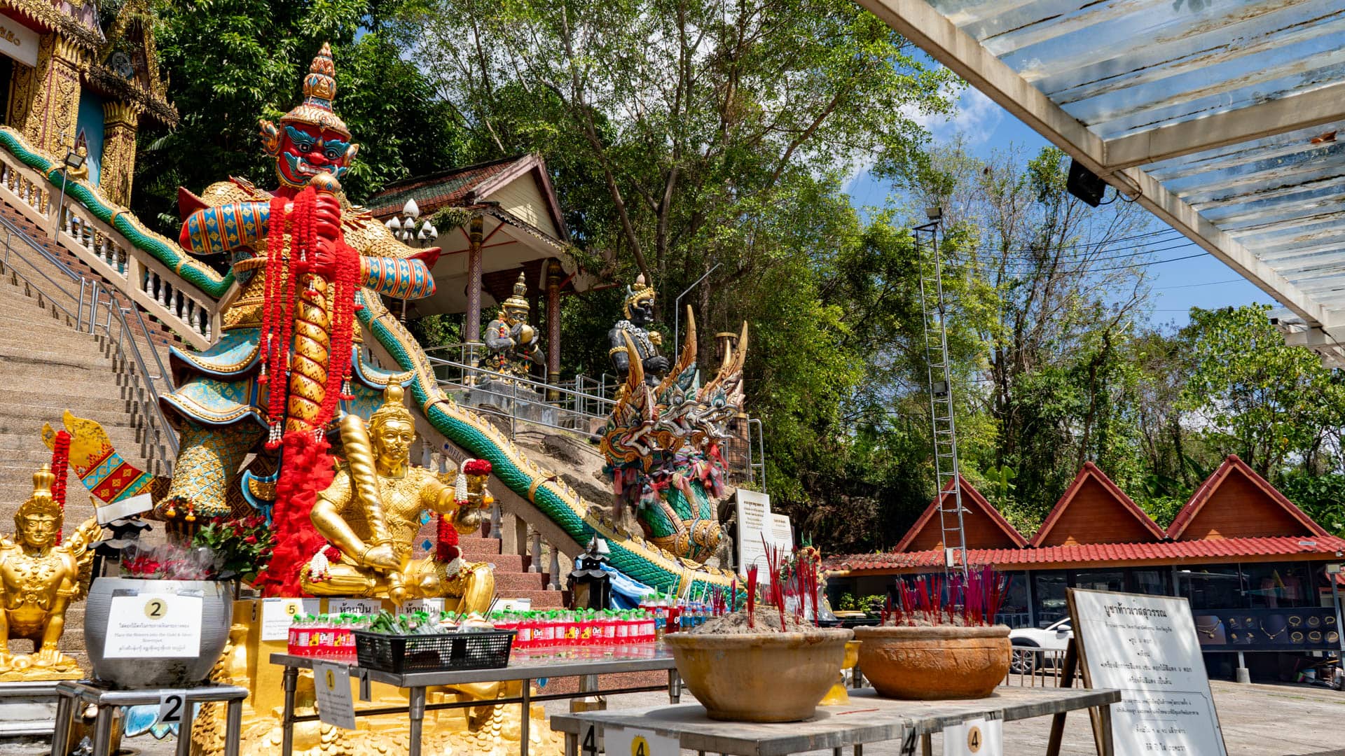 Incense burners and offering tables below guardian statue at temple stairway