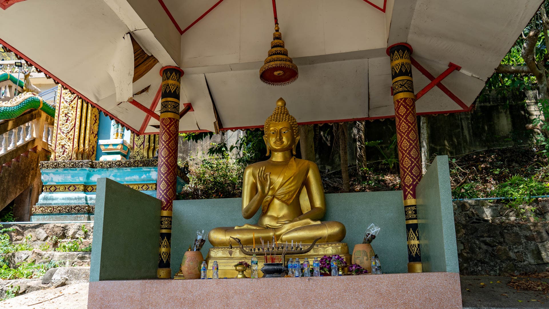Seated Buddha statue inside pavilion shrine beside temple stairway