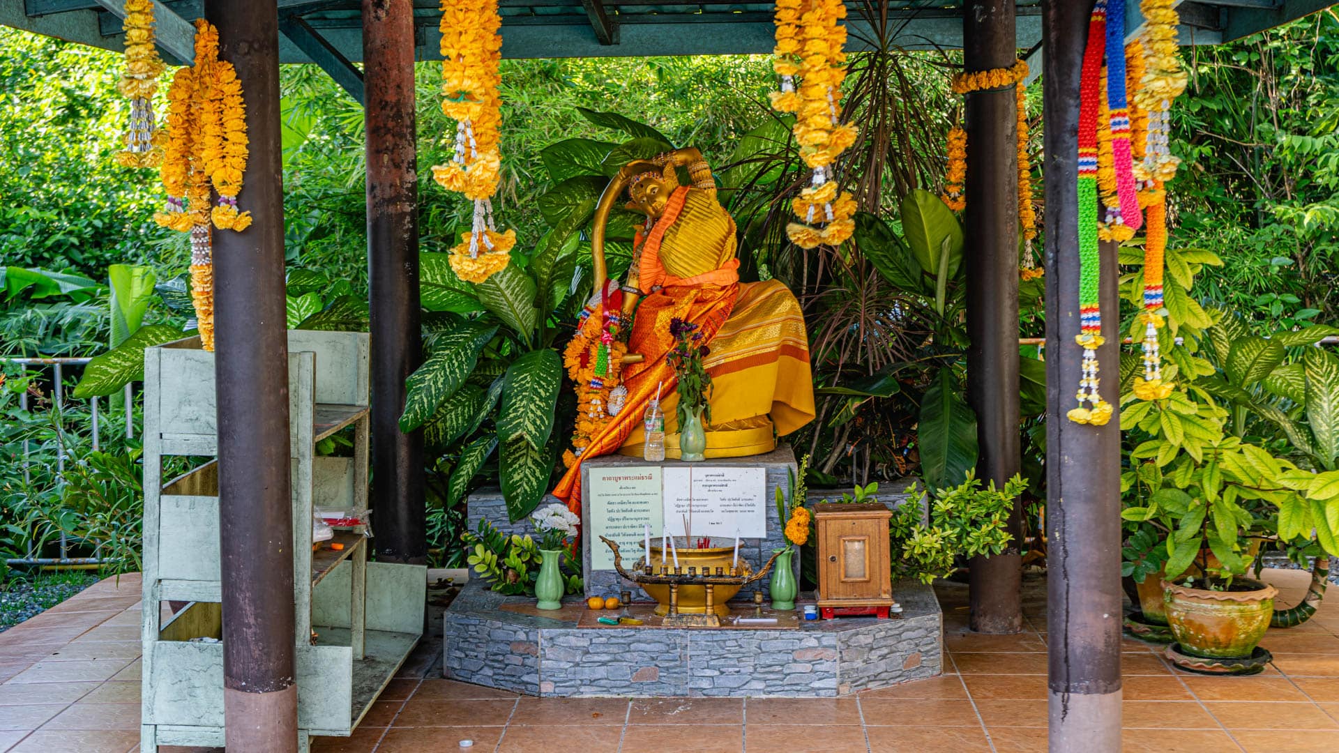 Garlanded shrine figure beneath blue roof with plants around it