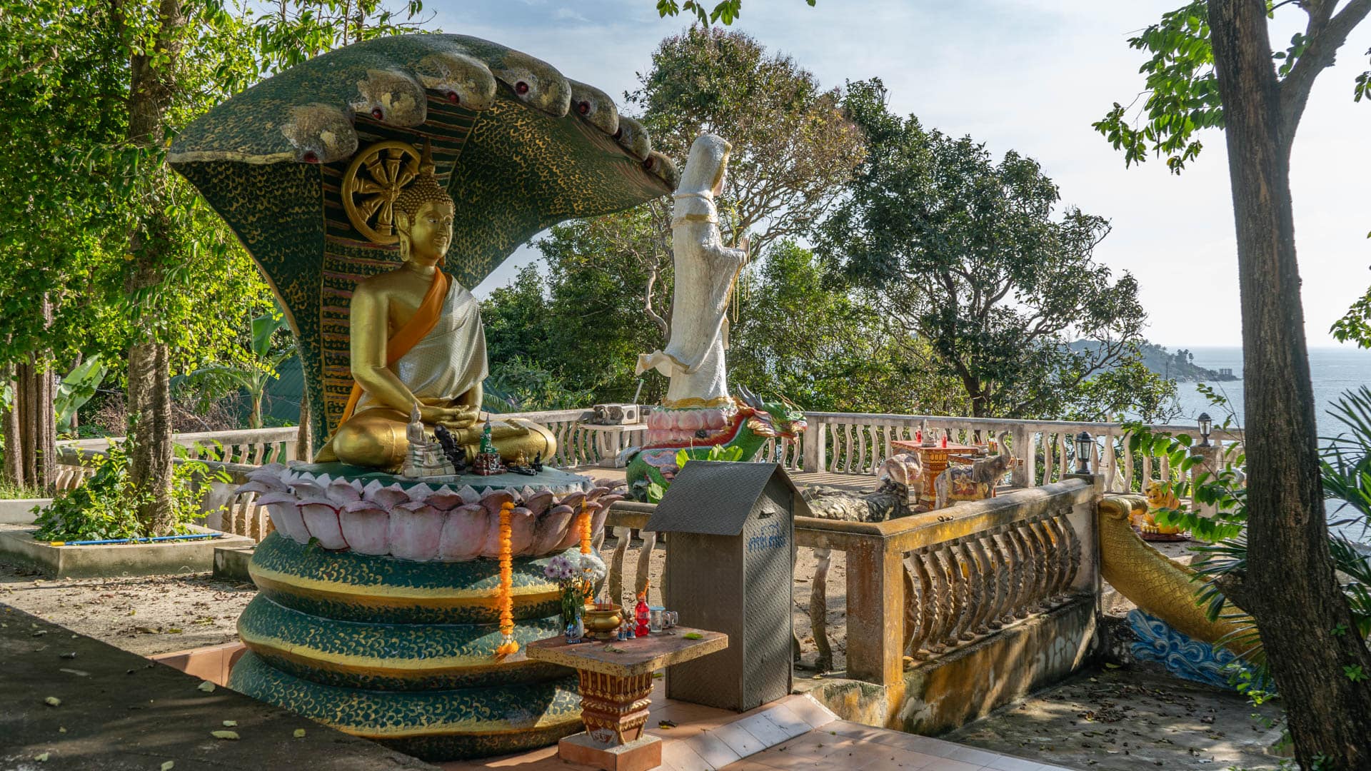 Seated Buddha beneath naga canopy on terrace above the sea
