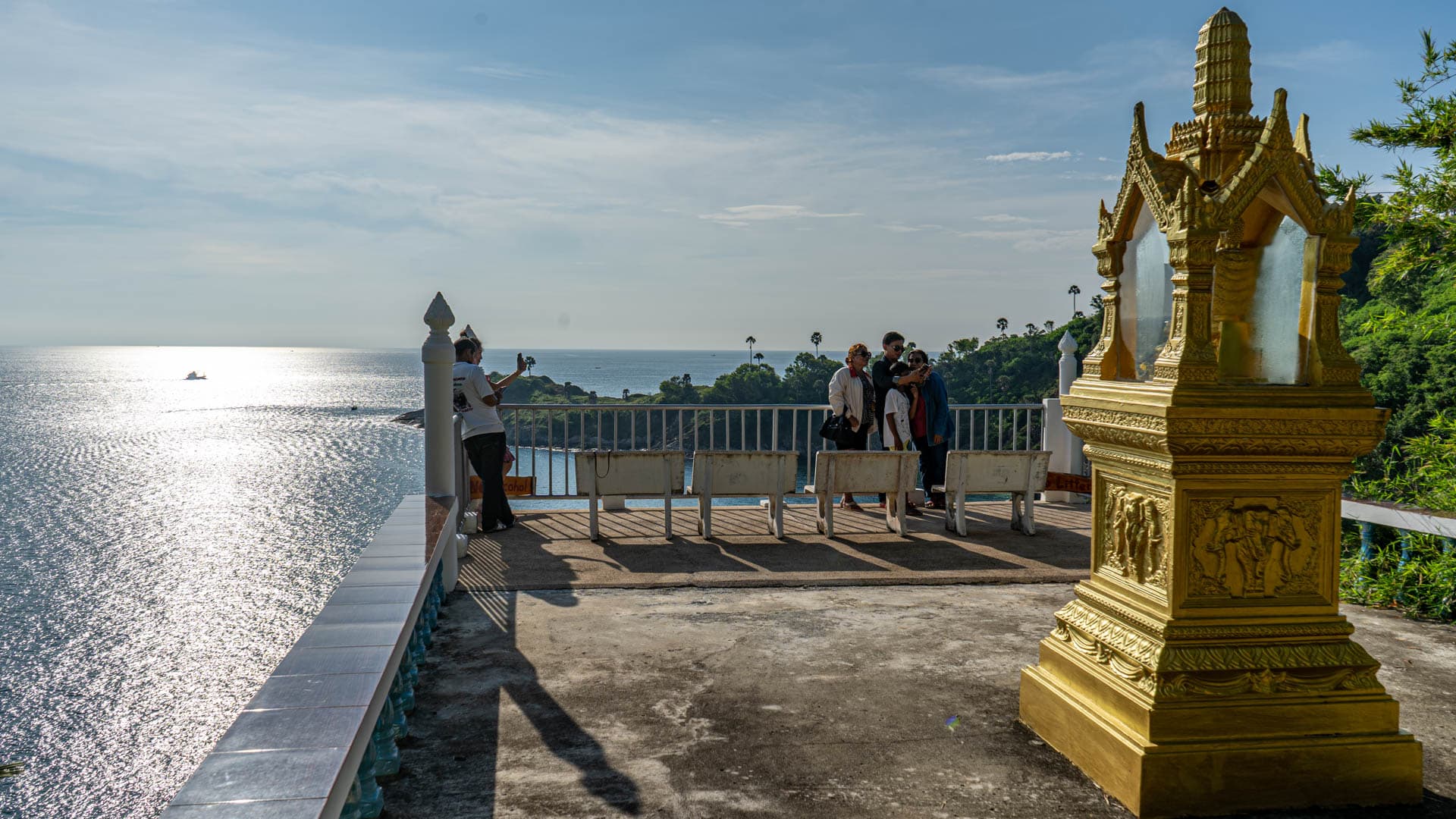 Visitors on terrace beside gilded shrine above bay at Wat Laem Phromthep