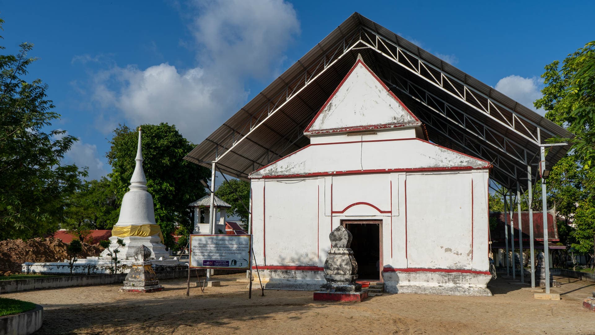 Old ordination hall and white chedi under protective roof structure