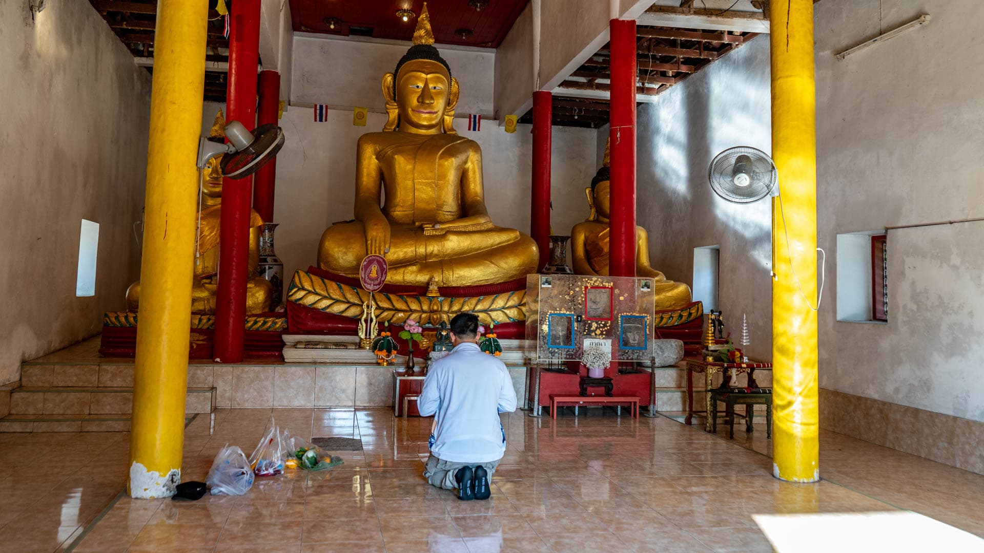Worshipper kneeling before three seated Buddha images inside the old hall