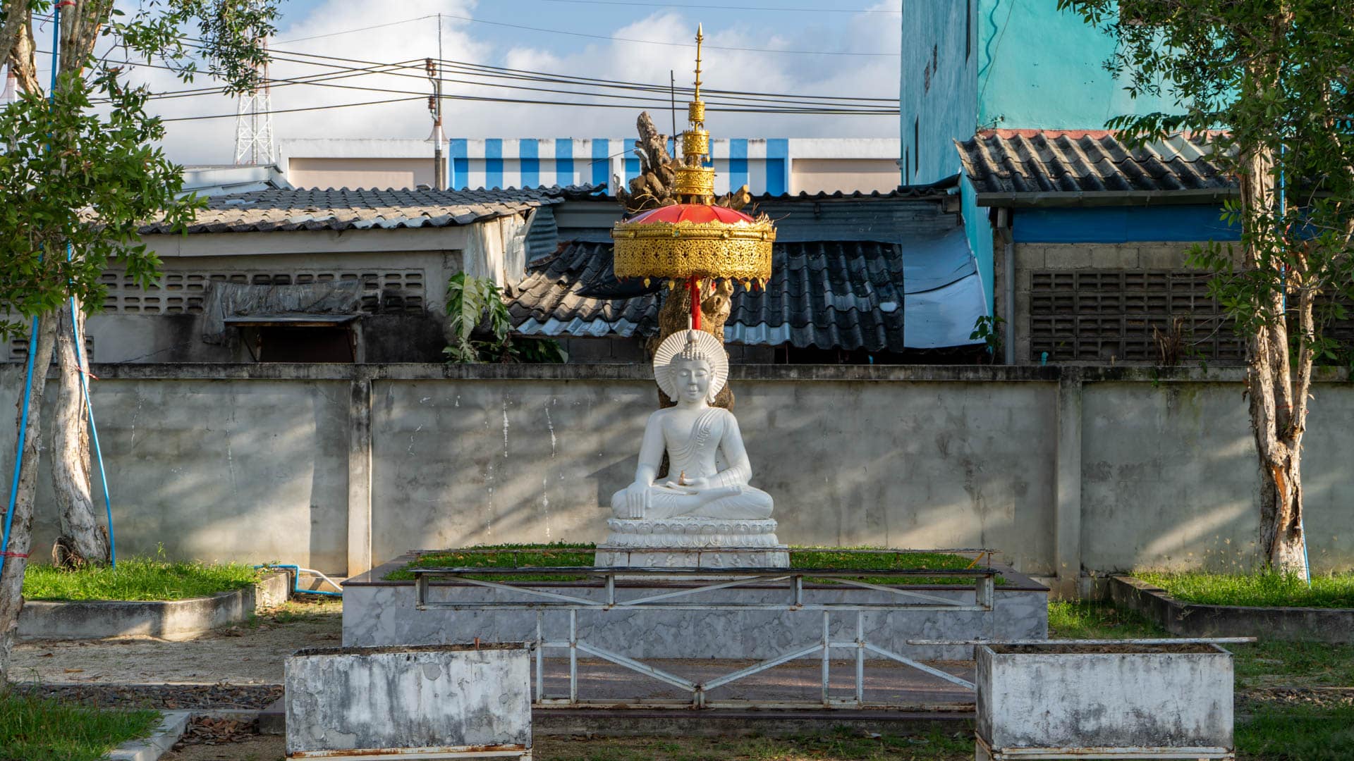 White seated Buddha statue beneath gilded parasol on outdoor pedestal