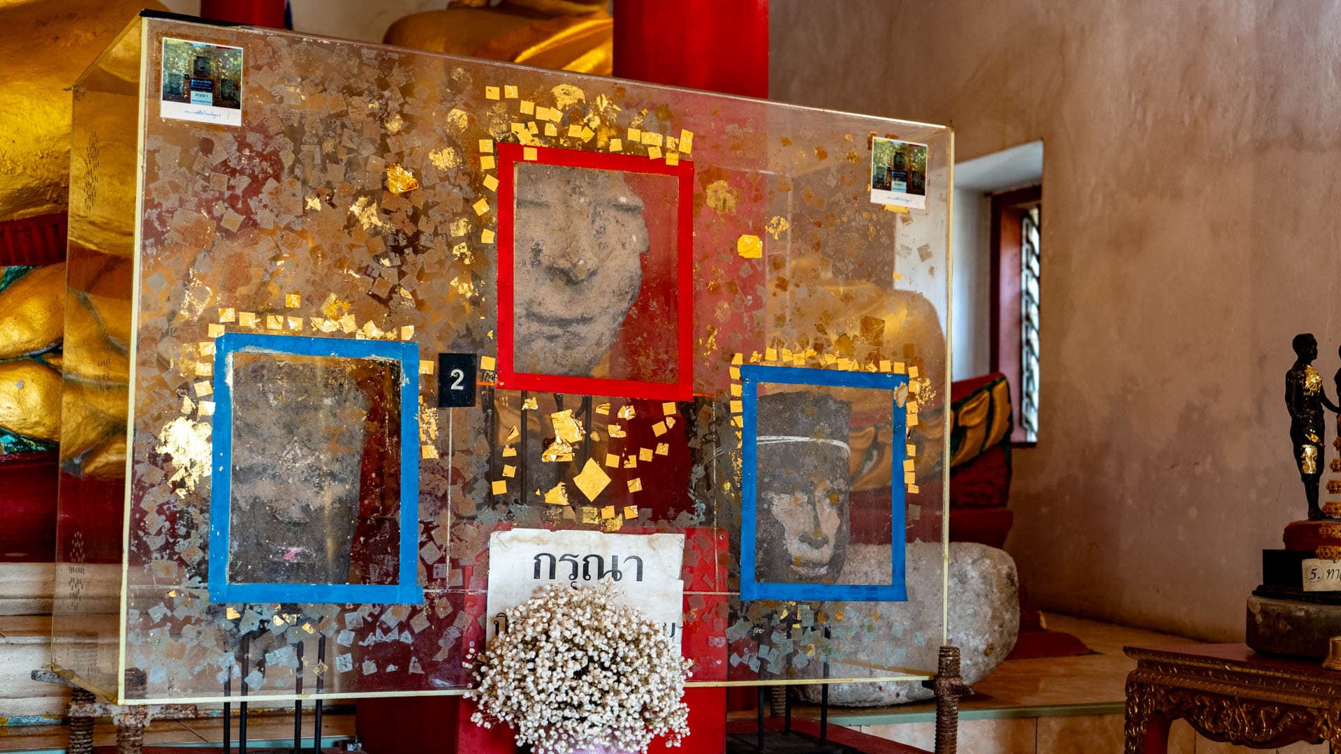 Glass case showing worn Tin Buddha heads inside the old ordination hall