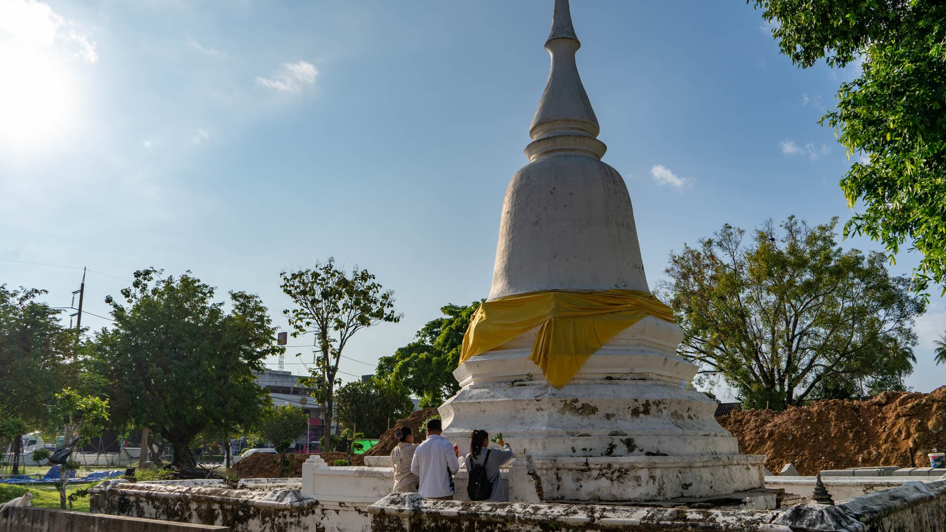 Three visitors beside white chedi wrapped with yellow cloth at temple