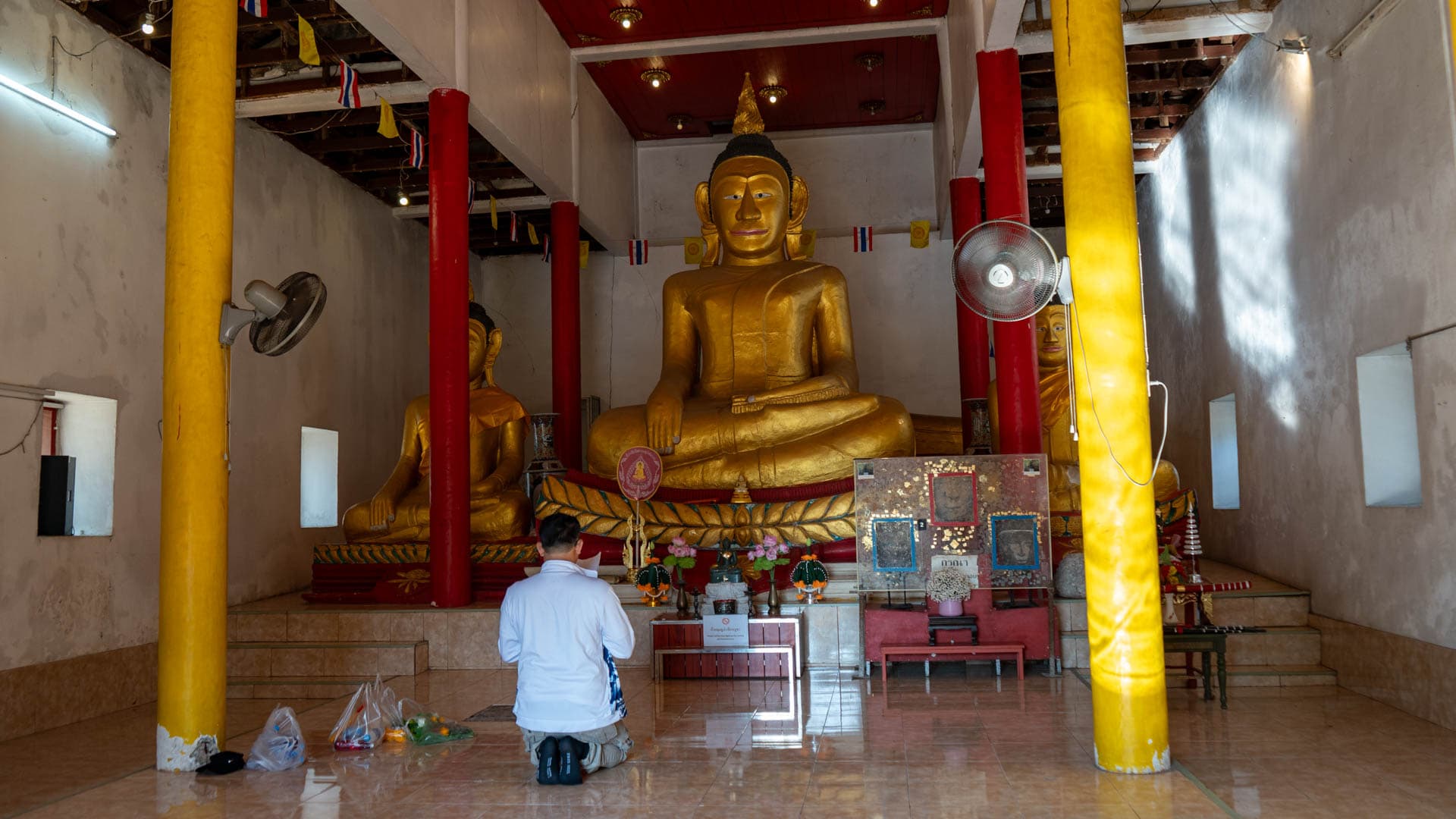 Worshipper facing Buddha images and display case inside the old hall
