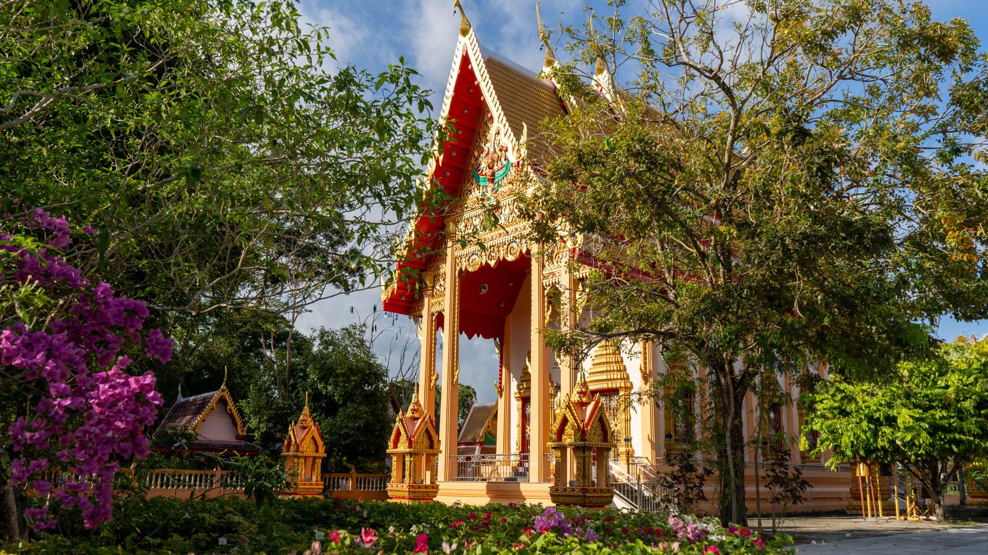 Main temple hall behind flower beds and trees at Wat Phra Thong