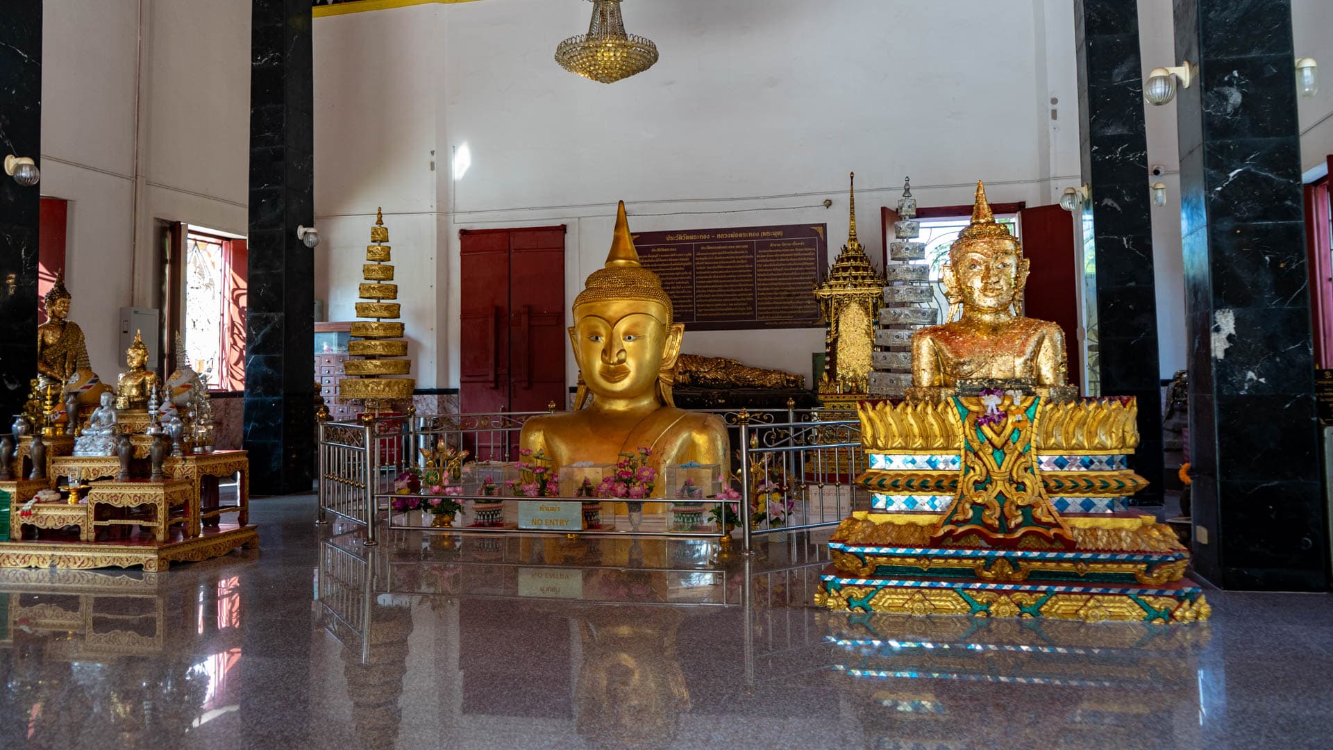 Half-buried Buddha image inside Wat Phra Thong hall with railings and offerings