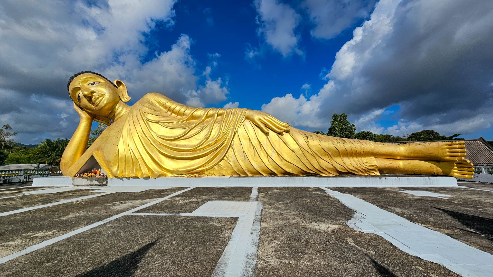 Large reclining Buddha statue on terrace at Wat Sri Sunthon under clouds
